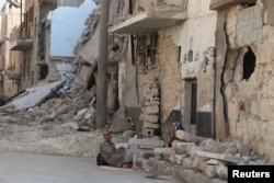Residents rest on the ground near rubble in a damaged neighbourhood in Aleppo, Syria, July 30, 2015.