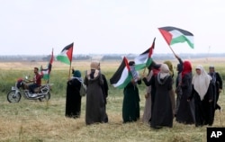 Female protesters wave their national flags while stand in front of Israeli soldiers during a demonstration along the Gaza Strip border with Israel, east of Khan Younis, Gaza Strip, Friday, March 30, 2018. (AP Photo/Adel Hana)
