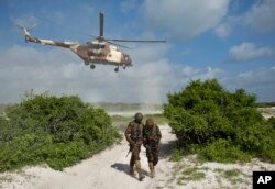 FILE - Two Kenyan army soldiers shield themselves from the downdraft of a Kenyan air force helicopter near the seaside town of Bur Garbo, Somalia, Dec. 14, 2011. A Kenyan military spokesman is categorically denying accusations that the Kenyan air force has been conducting airstrikes against Somali civilians.