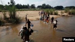 FILE - A group of Myanmar refugees, who crossed over from Myanmar to Thailand when a battle erupted between Myanmar's soldiers and rebels, walk across a stream of water at the Thai border town of Mae Sot, Nov. 8, 2010.