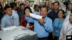In this Sunday, July 29, 2018, file photo, Cambodian Prime Minister Hun Sen, center, of the Cambodian People's Party (CPP), holds a ballot before voting at a polling station in Takhmua in Kandal province, southeast of Phnom Penh, Cambodia.