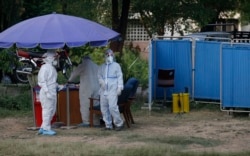 Health workers wait for people to collect samples at a drive-through testing and screening facility for the coronavirus, in Islamabad, Pakistan, Saturday, June 6, 2020.