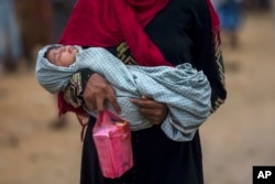 FILE - A Rohingya Muslim woman, who crossed over from Myanmar into Bangladesh, holds her sick daughter and some medicine and walks back toward her shelter in Thaingkhali refugee camp, Bangladesh, Oct. 21, 2017.