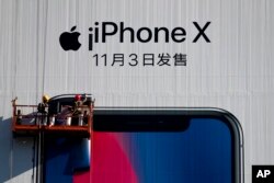 Workers on a suspended platform replace an advertisement poster for the new iPhone X on a building in Beijing, Oct. 30, 2017.