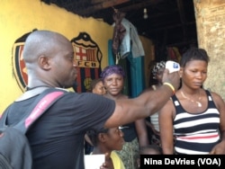 Sulaiman Watfa, an Ebola survivor, takes the temperature of resident Fatmata Bangura in the community of Moa Wharf, Sierra Leone, May 27, 2015.