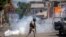 FILE - A police officer runs away from tear gas during a protest to demand the resignation of Haiti's president Jovenel Moise in Port-au-Prince, Haiti, Feb. 10, 2021. 