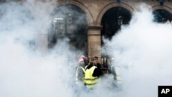 Para demonstran (mengenakan rompi kuning) berjalan melewati bom asap di dekat kebun Tuileries di Paris, Sabtu, 22 Desember 2018. (Foto: dok).