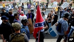 A white supremacist carries the Confederate flag as he walks past counterdemonstrators in Charlottesville, Va., Aug. 12, 2017. 