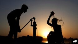A Pakistani youth, right, cools off under a hand pump at sunset during hot weather in Lahore, Pakistan, May 28, 2024. 
