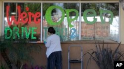 Lucy Kwak paints a sign on the window of a fast-food chain's restaurant indicating that the drive-through window is still open as well as a takeout option during the coronavirus outbreak in Garden Grove, Calif., March 26, 2020.