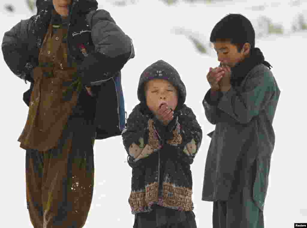 Anak-anak keluar dari tempat tinggal mereka di sebuah kamp pengungsi, saat salju turun di Kabul, Afghanistan.