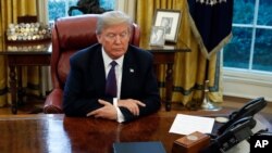 FILE - President Donald Trump sits over documents at his desk in the Oval Office of the White House, in Washington, Jan. 23, 2018. 