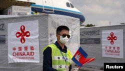 បុគ្គលិកប្រចាំអកាសយានដ្ឋានអន្តរជាតិភ្នំពេញម្នាក់កាន់ទង់ជាតិកម្ពុជា និងចិន ខណៈយន្តហោះដឹកក្រុមគ្រូពេទ្យចិន និងសម្ភារៈបរិក្ខាពេទ្យពីប្រទេសចិន បានមកដល់កម្ពុជា ដើម្បីជួយកម្ពុជាក្នុងការប្រយុទ្ធនឹងការឆ្លងរាលដាលនៃវីរុសកូរ៉ូណា ឬកូវីដ១៩ នៅរាជធានីភ្នំពេញ ថ្ងៃទី២៣ ខែមីនា ឆ្នាំ២០២០។