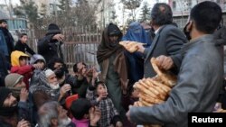 Seorang perempuan Afghanistan menerima bantuan sepotong roti di depan toko roti di antara kerumunan di Kabul, Afghanistan, 31 Januari 2022. (Foto: REUTERS/Ali Khara)