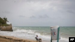A man sits in front of a beach watching as the waves break before the arrival of Tropical Storm Fiona in San Juan, Puerto Rico, Sept. 17, 2022. 