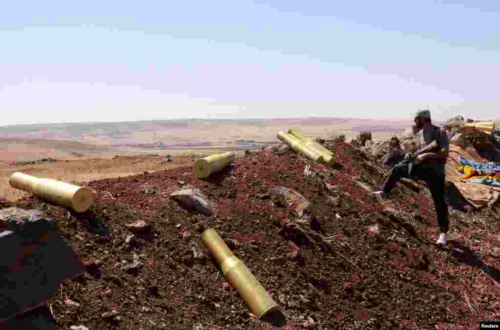A man belonging to forces loyal to Syria's President Bashar al-Assad stands next to spent ammunition rounds in Tal El-Tineh village outside Aleppo, Syria, June 16, 2013.