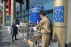 FILE - Bhutanese people wash their hands before entering their office as a precaution against the COVID-19 in Thimpu, April 12, 2021.