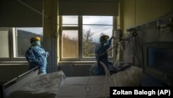 In this March 24, 2020, file photo, medical staff members check a ventilator in protective suits at the care unit for the new COVID-19 infected patients inside the Koranyi National Institute of Pulmonology in Budapest. (Zoltan Balogh/MTI via AP, File)