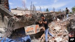Seorang pria mengambil sebuah kotak makanan dari bawah reruntuhan bangunan pasca gempa yang menghantam wilayah Pidie Jaya, provinsi Aceh, Indonesia, 7 Desember 2016 (AP Photo/Heri Juanda).
