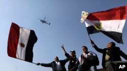 FILE - Egyptians wave national flags as they greet an army helicopter flying over Tahrir Square.
