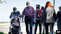 Maria and Philip Ptacin wear masks while taking a walk with their 17-month-old granddaughter, Juliette Hitchen, May 20, 2020, in Portland, Maine. 