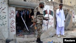 An army soldier stands with a police officer in front of a damaged Pakistan People's Party (PPP) election campaign office after a bomb blast, in Quetta, May 10, 2013.