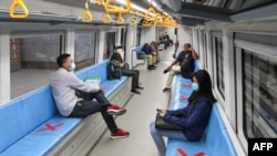 People sit on areas designated by red cross marks to ensure social distancing inside a light rapid transit train in Palembang, South Sumatra, Indonesia. 