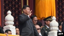 Presiden China Xi Jinping (kiri) melambaikan tangannya di sebelah mantan presiden Jiang Zemin (bawah kiri) selama parade militer di Beijing pada 1 Oktober 2019, menandai peringatan ke-70 berdirinya Republik Rakyat China. (Foto oleh Greg BAKER / AFP)