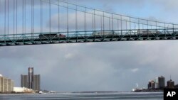 FILE- Cargo trucks cross the Ambassador Bridge from Detroit, left, leading into Windsor, Ontario, right, Jan. 6, 2015. Desperate immigrants are flowing across the U.S. border into Canada, increasingly being seen as a haven for asylum-seekers turned away by the U.S.