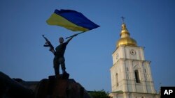 A woman brandishes the Ukrainian flag on top of a destroyed Russian tank in Kyiv, Ukraine, June 10, 2022.
