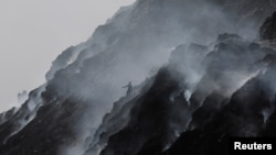 FILE - A waste collector climbs down while looking for recyclable materials as smoke billows from burning garbage at the Bhalswa landfill site on World Environment Day in New Delhi, India, June 5, 2022. (REUTERS/Anushree Fadnavis)