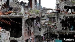 FILE - A woman stands at her ruined house, after residents were allowed to return to their homes for the first time since the battle between government troops and Islamic State militants began on May 2017, at the Islamic city of Marawi, Philippines, April 19, 2018.