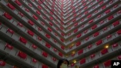 A woman walks past the Chinese and Hong Kong flags hanging from a residential building to celebrate the 25th anniversary of Hong Kong handover to China, at a public housing estate, in Hong Kong, Saturday, June 25, 2022.