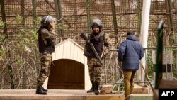 Des paramilitaires des Forces auxiliaires marocaines parlent avec un homme alors qu'ils montent la garde près de la barrière frontalière séparant le Maroc de l'enclave nord-africaine de Melilla en Espagne.