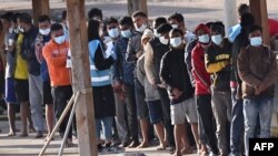 FILE - Migrants line up after disembarking on the southern Italian island of Lampedusa on May 17, 2021.