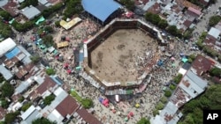 In this image taken from video, spectators gather around the wooden stands that collapsed during a bullfight in El Espinal, Tolima state, Colombia, Sunday, June 26, 2022. According to authorities, the collapse sent spectators plunging to the ground, killing at least four.