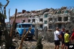 Local residents stand next to a damaged residential building in the town of Serhiivka, about 50 kilometers southwest of Odesa, Ukraine, July 1, 2022.