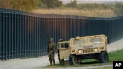 FILE - National Guardsmen stands watch over a fence near the International Bridge, in Del Rio, Texas, on Sept. 18, 2021. 