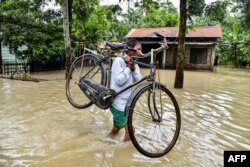 A man carries his bicycle as he wades through flood waters in Solmara of Nalbari district, in India's Assam state on June 19, 2022.
