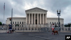 People walk dogs past anti-scaling fencing erected around the U.S. Supreme Court in Washington, June 23, 2022. (AP Photo/Gemunu Amarasinghe)