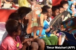 Anak-anak menonton mantan guru Samsudin saat mengajar mereka tentang konservasi hewan dengan boneka kardus di desa Cemara Kulon, Indramayu. (Foto: AFP/Timur Matahari)