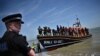 FILE - A British police officer stands guard on the beach of Dungeness, on the southeast coast of England, on June 15, 2022, as migrants disembark from a lifeboat after they were picked up at sea while attempting to cross the English Channel.