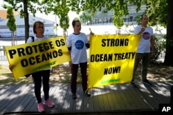 FILE - Greenpeace activists hold banners outside the venue, in the background, hosting the United Nations Ocean Conference in Lisbon, June 30, 2022.