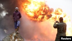Seorang pria mengambil foto temannya saat asap tebal membumbung dari kebakaran yang terjadi di sumur-sumur minyak yang dibakar oleh kaum militan Islamic State sebelum mereka meninggalkan kawasan produsen minyak Qayyara, Irak (28/1). (foto: REUTERS/Muhammad Hamed)