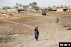 A woman walks to fetch water from a nearby hand-pump with a water cooler on her head, during a heatwave, on the outskirts of Jacobabad, Pakistan, May 16, 2022. (REUTERS/Akhtar Soomro)