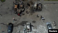 People stand next to cars destroyed by a Russian missile strike at a residential area in Kharkiv, Ukraine, June 26, 2022. 