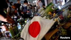 A Japanese flag is seen as people pray next to tributes laid at the site where late former Japanese Prime Minister Shinzo Abe was shot while campaigning for a parliamentary election, near Yamato-Saidaiji station in Nara, western Japan, July 8, 2022.