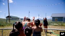 Tyisha ArrowTop Knot, right, sprays her nieces and nephews with a garden hose while looking after them in the backyard of their home on the Blackfeet Indian Reservation in Browning, Mont., Thursday, July 12, 2018.