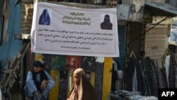 Seorang perempuan yang mengenakan burkak berjalan melintasi spanduk di Kandahar, Afghanistan, pada 16 Juni 2022. Spanduk yang dipasang oleh Taliban itu berisi perintah bagi perempuan untuk mengenakan hijab. (Foto: AFP/Javed Tanveer)