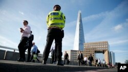Para pejalan kaki berjalan melewati seorang polisi di London Bridge, London, 7 JUni 2017 (AP Photo/Alastair Grant).